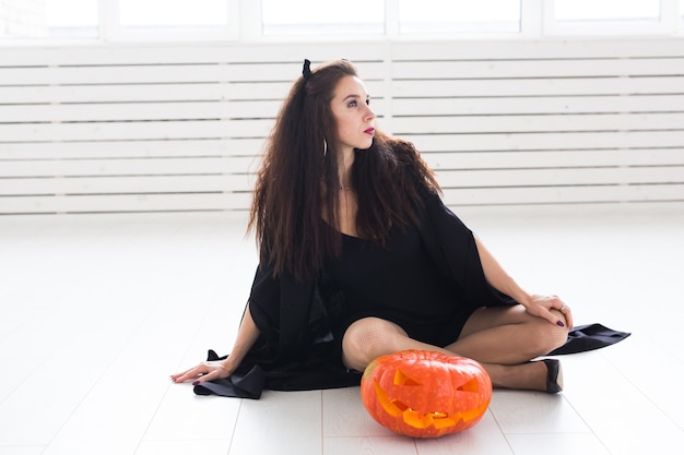 Donna castana sorridente nel trucco di halloween che posa con la zucca intagliata.