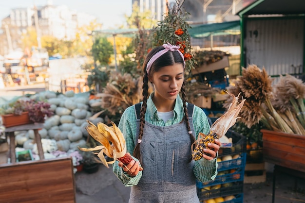 Donna casual attraente che compra con gioia il mais colorato al mercato