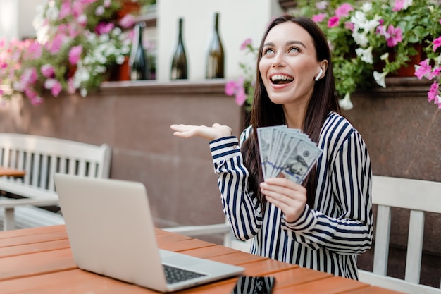 Donna casuale con soldi facendo uso del computer portatile nel ristorante