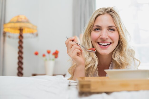 Donna casuale felice che mangia alimento a letto