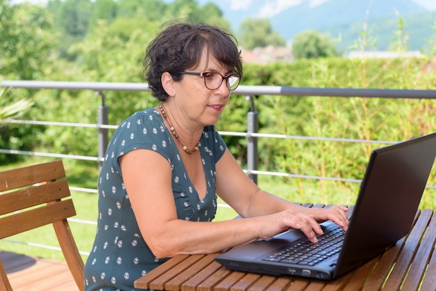 Donna casuale moderna che si siede al giardino con il computer portatile