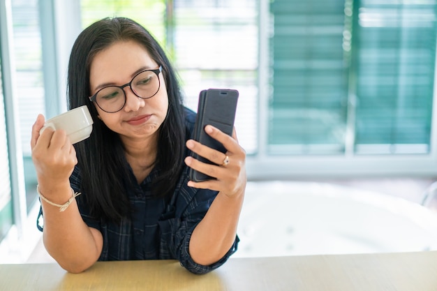 Donna casuale noiosa che parla sopra il telefono cellulare con la tazza di caffè a disposizione