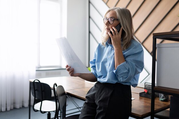 Donna caucasica adulta matura di affari che parla sul telefono cellulare mentre esamina i documenti mentre