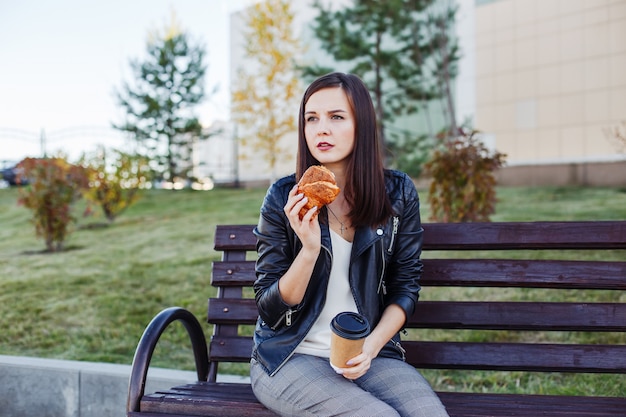 Donna caucasica bella che si siede nel parco e che mangia croissant