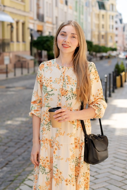 Donna caucasica bionda in abito colorato e con caffè da asporto sullo sfondo della strada