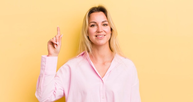 Donna caucasica bionda sorridente allegramente e felicemente rivolta verso l'alto con una mano per copiare lo spazio