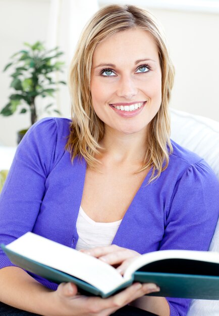 Donna caucasica brillante che legge un libro che si siede su un sofà