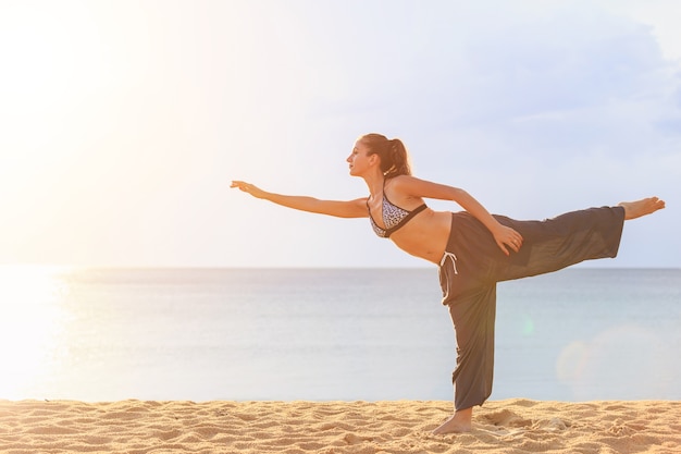 Donna caucasica che gioca yoga ed esercizio sulla spiaggia tropicale