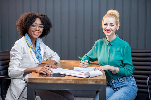 Donna caucasica che ha una consultazione medica seduta con un medico di etnia afro presso l'ufficio moderno