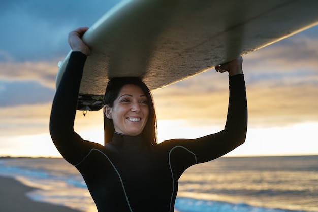 Donna caucasica che indossa una tuta da surf con una tavola da surf sorridente felicemente