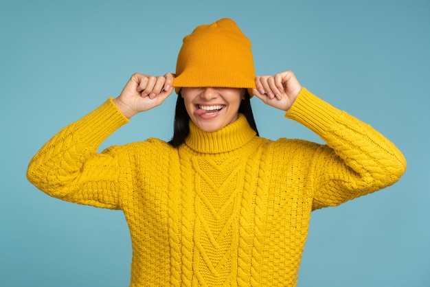 Donna caucasica che si sente benissimo durante il gelo che indossa un maglione giallo e un cappello caldo e mostra la lingua con umore divertente