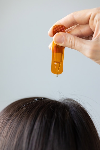 Donna caucasica che tiene in mano una fiala di vitamine e si applica ai capelli o alla pelle del primo piano dei capelli e della pelle