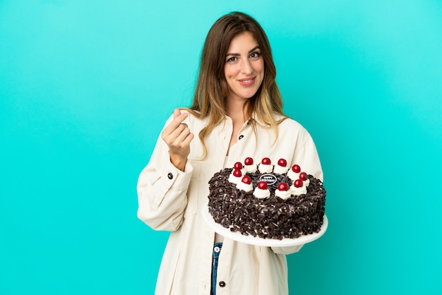 Donna caucasica che tiene la torta di compleanno isolata su fondo blu che fa i soldi gesture