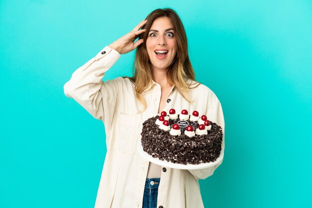 Donna caucasica che tiene la torta di compleanno isolata su fondo blu con l'espressione di sorpresa