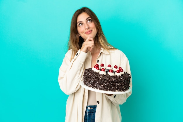 Donna caucasica che tiene la torta di compleanno isolata su fondo blu e che guarda in su