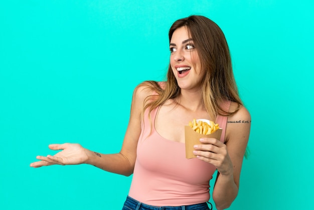 Donna caucasica che tiene patatine fritte isolate su sfondo blu con espressione di sorpresa mentre guarda di lato