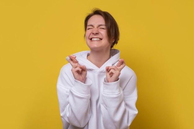 Donna caucasica chiudendo gli occhi incrociando le dita sperando per il miglior Studio girato sul muro giallo