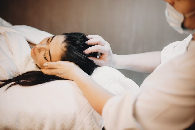 Donna caucasica con capelli neri che ha una procedura termale di massaggio alla testa presso il salone professionale