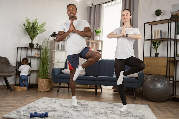 Donna caucasica con il marito africano che fa allenamento fitness mentre il figlio gioca sul pavimento