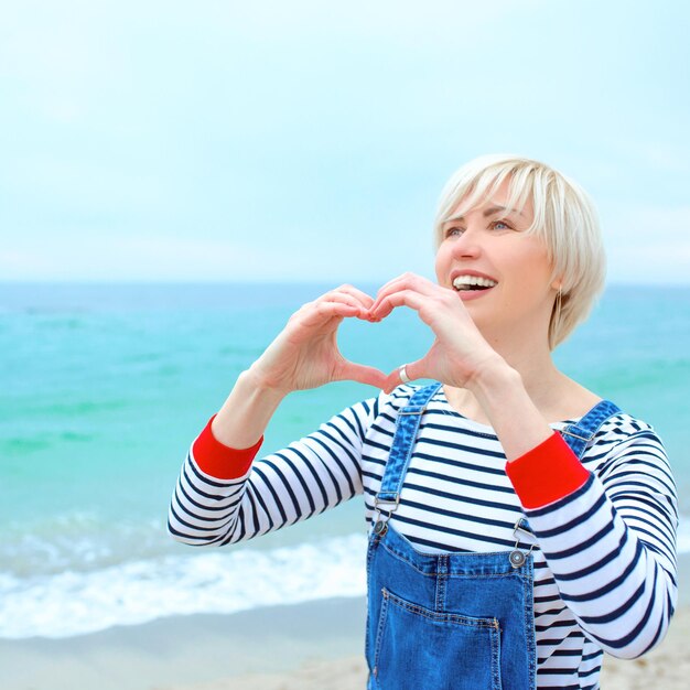 donna caucasica con le mani come segno d'amore in vacanza al mare