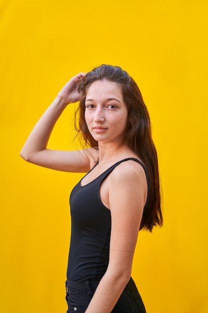 donna caucasica con lunghi capelli castani, vestita di canotta nera e jeans neri, toccandosi i capelli