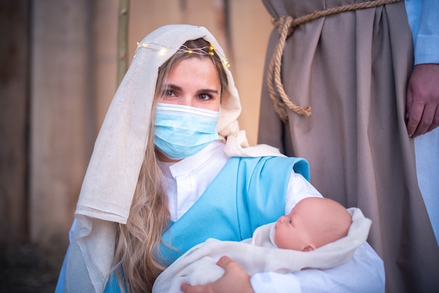 Donna caucasica con maschera che rappresenta la Vergine Maria di fronte alla telecamera mentre tiene in braccio un bambino in una culla