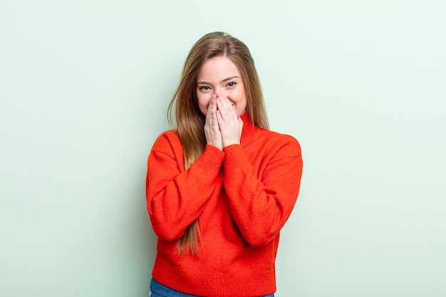 Donna caucasica dai capelli rossi che sembra felice, allegra, fortunata e sorpresa che copre la bocca con entrambe le mani