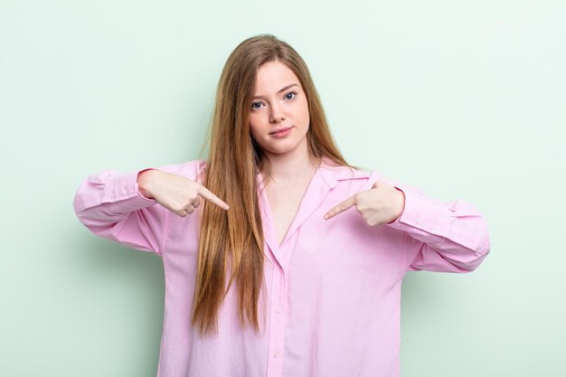 Donna caucasica dai capelli rossi che sembra orgogliosa, positiva e casual che punta al petto con entrambe le mani