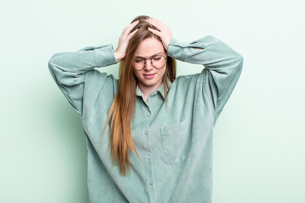 donna caucasica dai capelli rossi che si sente stressata e frustrata, alza le mani alla testa, si sente stanca, infelice e con emicrania