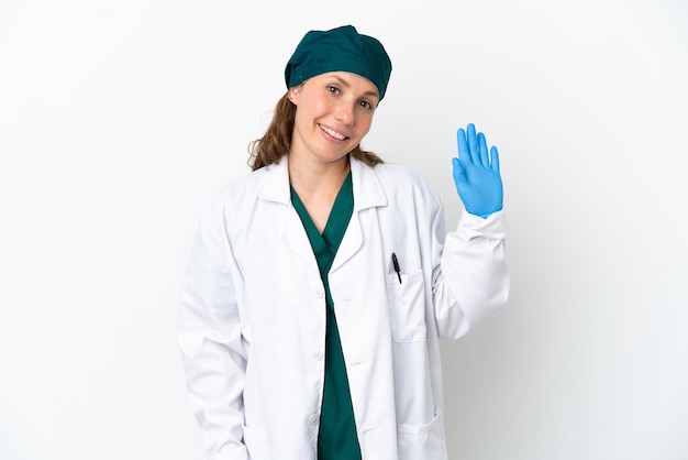 Donna caucasica del chirurgo in uniforme verde isolata su fondo bianco che saluta con la mano con l'espressione felice