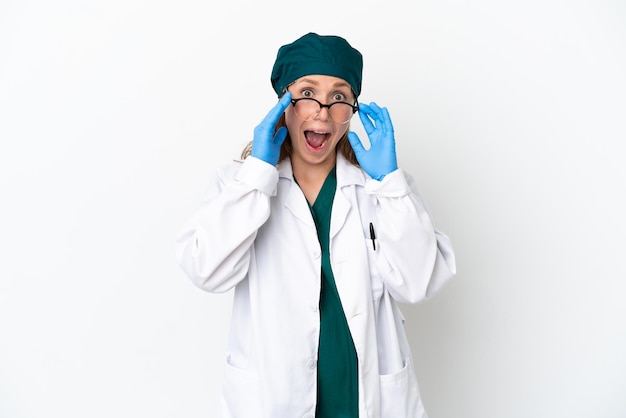 Donna caucasica del chirurgo in uniforme verde isolata su fondo bianco con gli occhiali e sorpresa