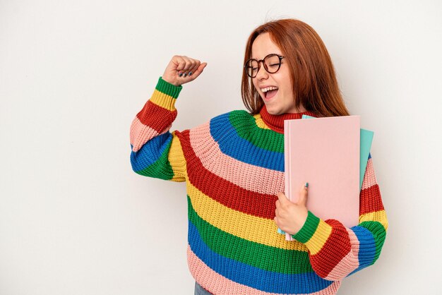 Donna caucasica del giovane studente isolata su fondo bianco che alza il pugno dopo una vittoria, concetto del vincitore.