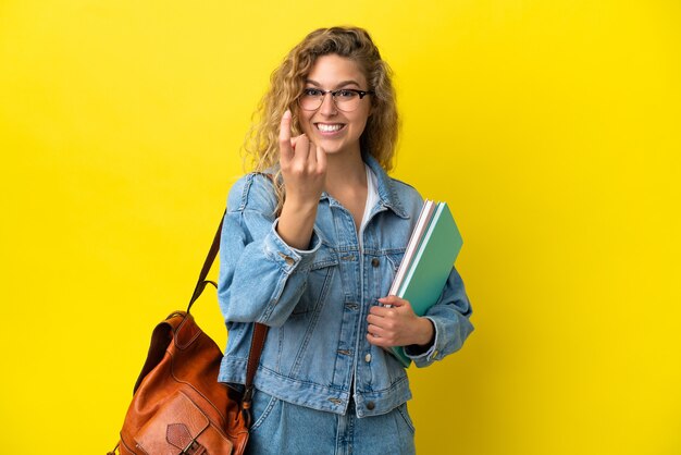 Donna caucasica del giovane studente isolata su fondo giallo che fa il gesto venente