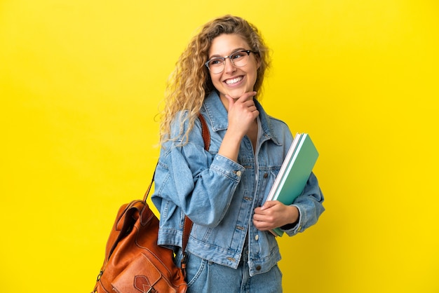 Donna caucasica del giovane studente isolata su fondo giallo che guarda al lato e che sorride