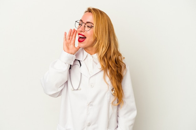 Donna caucasica del medico isolata su fondo bianco che grida e che tiene il palmo vicino alla bocca aperta.