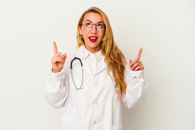 Donna caucasica del medico isolata su fondo bianco che indica al rialzo con la bocca aperta.