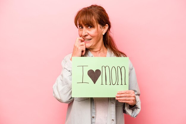 Donna caucasica di mezza età che tiene il cartello I love mom isolato su sfondo rosa rilassato pensando a qualcosa guardando uno spazio di copia