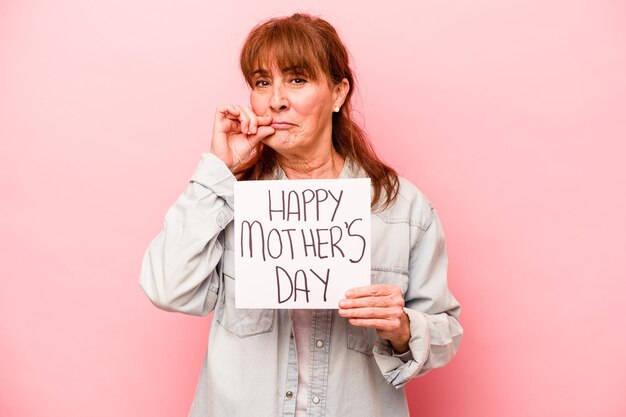 Donna caucasica di mezza età che tiene il cartello per la festa della mamma felice isolato su sfondo rosa con le dita sulle labbra che mantengono un segreto