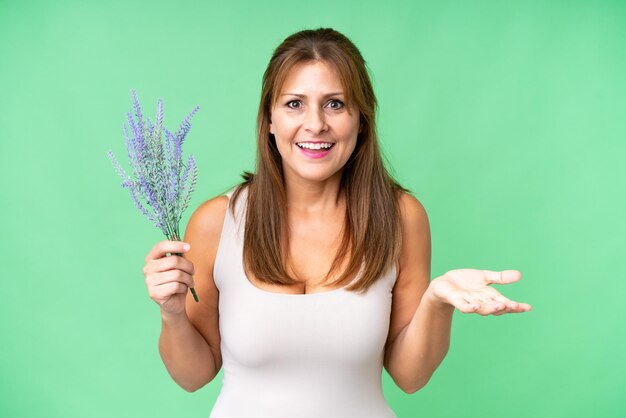 Donna caucasica di mezza età che tiene lavanda su sfondo isolato con espressione facciale scioccata