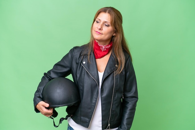 Donna caucasica di mezza età con un casco da motociclista su sfondo isolato guardando di lato e sorridente