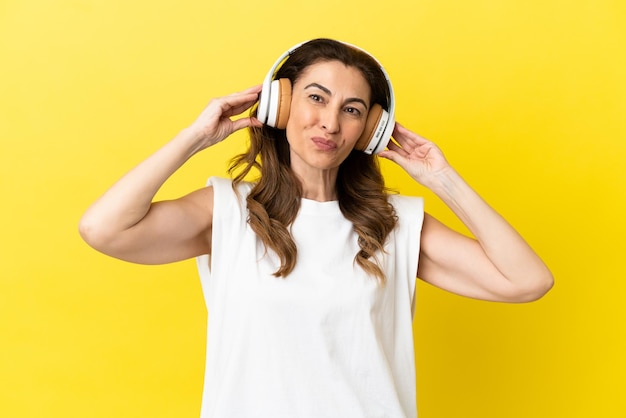 Donna caucasica di mezza età isolata su sfondo giallo che ascolta musica