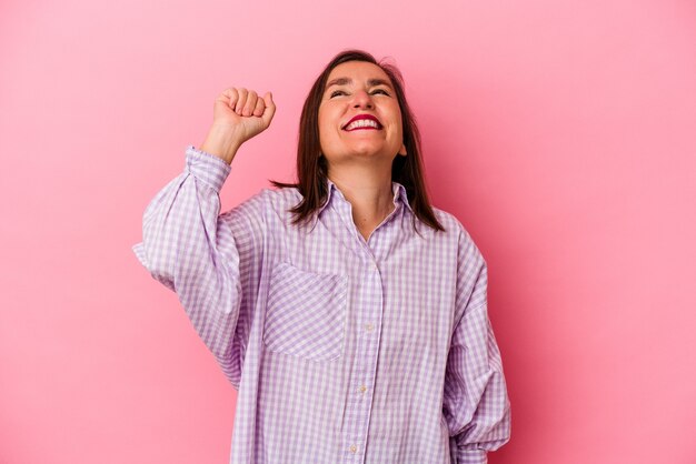 Donna caucasica di mezza età isolata su sfondo rosa che celebra una vittoria, passione ed entusiasmo, espressione felice.