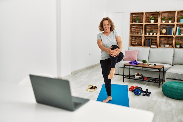 Donna caucasica di mezza età sorridente fiducioso utilizzando il computer portatile che si estende a casa