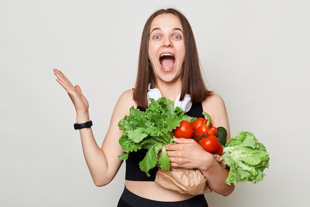 Donna caucasica eccitata stupita che tiene in piedi verdure biologiche isolate su sfondo bianco urlando di felicità esultando per la nuova stagione di cibo vegano fresco