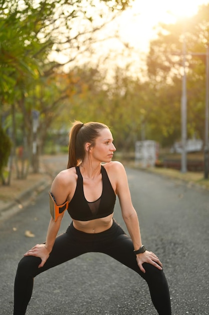 Donna caucasica fitness attiva che si allunga e si riscalda prima degli esercizi nel parco con luce solare intensa sullo sfondo