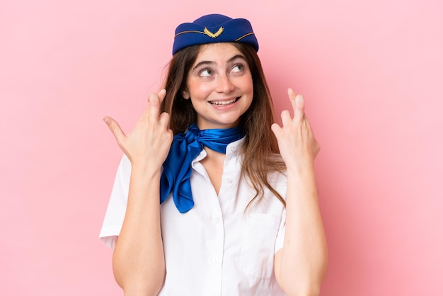Donna caucasica hostess dell'aeroplano isolata su sfondo rosa con le dita incrociate