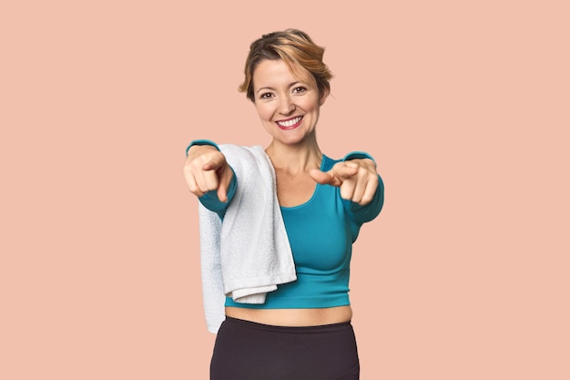 Donna caucasica in abbigliamento sportivo con asciugamano sorrisi allegri che indicano la parte anteriore
