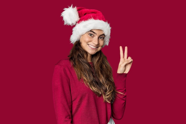 Donna caucasica in abito natalizio e cappello di Babbo Natale gioiosa e spensierata che mostra un simbolo di pace