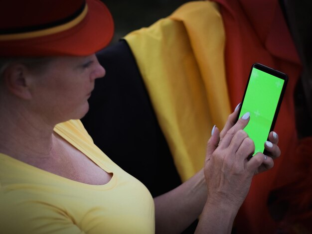 Donna caucasica in parrucca bandiera belga che tiene smartphone con schermo verde