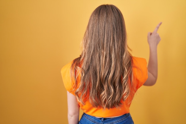 Donna caucasica in piedi su sfondo giallo in posa all'indietro che punta in avanti con la mano del dito